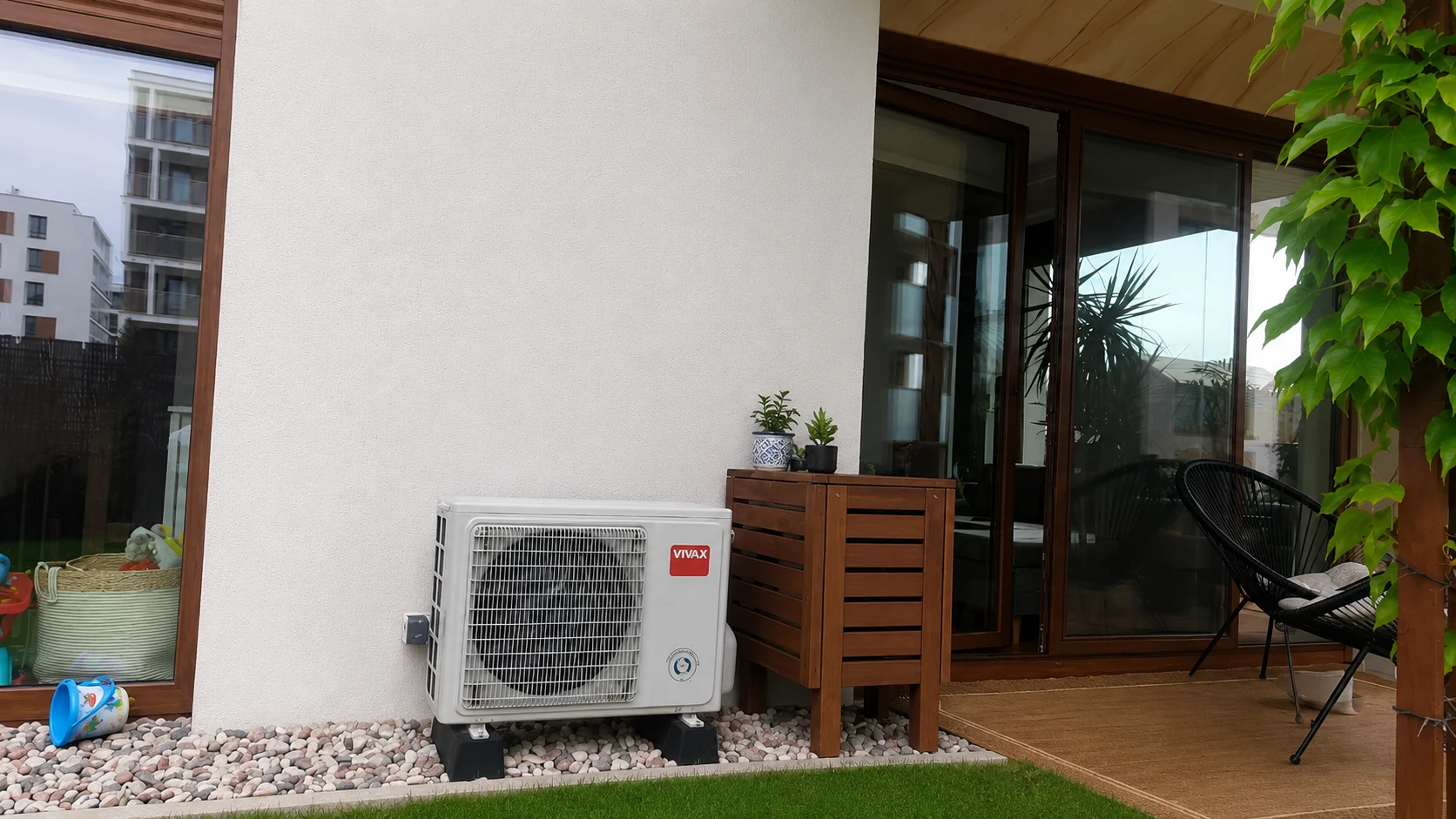 Jednostka zewnętrzna klimatyzatora przy tarasie, na podstawach wśród ozdobnych kamieni.
